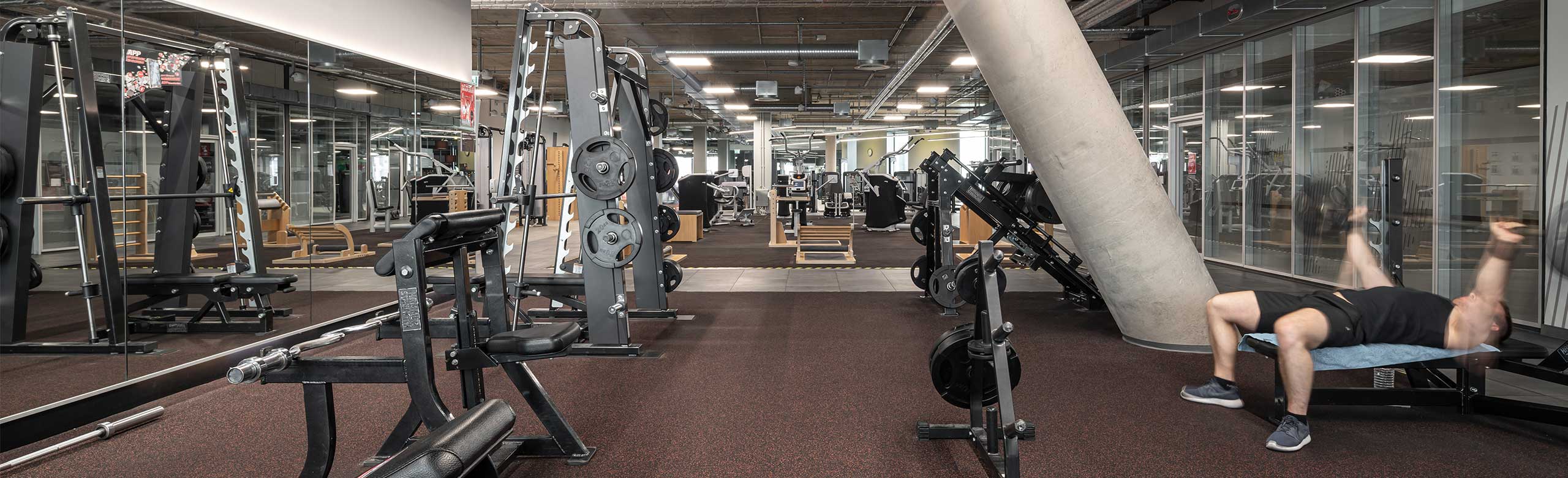 Podłoga REGUPOL w strefie treningu z wolnymi ciężarami w centrum fitness. Widać mężczyznę leżącego na ławce do podnoszenia ciężarów.