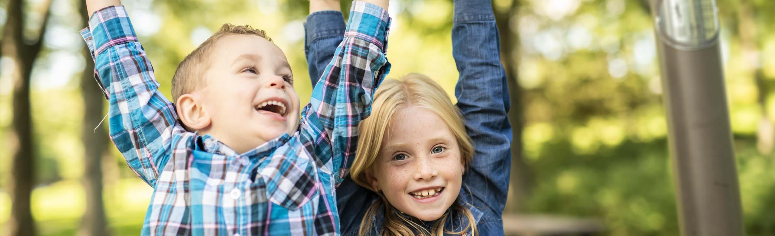 REGUPOL playfix elastic tiles on multifunctional playgrounds - for safety and play comfort Children play safely on a colourful multifunctional play area with REGUPOL playfix elastic tiles, surrounded by trees.