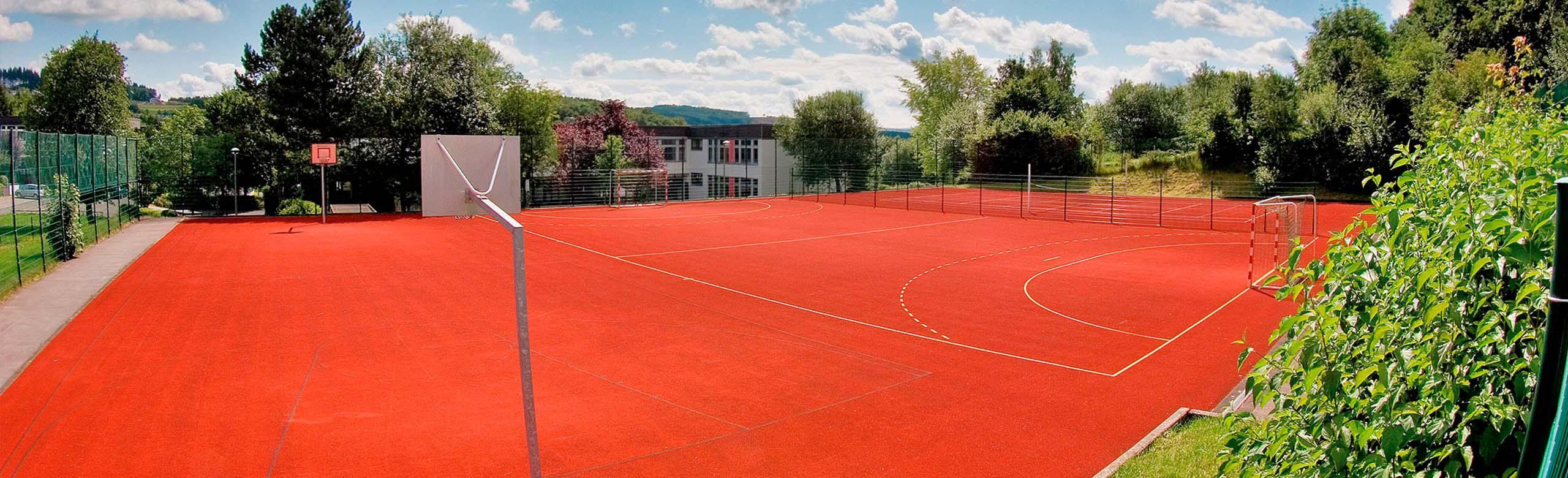 REGUPOL playfix game - High-quality, shock-absorbing sports surface for outdoor playing fields Barrier-free multifunctional outdoor playing field with red REGUPOL playfix game surface for all leisure and sports activities, surrounded by nature